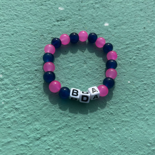 Bracelet with blue and pink beads and letter beads on a textured green surface